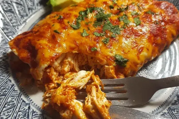 High protein chicken enchiladas topped with melted cheese and cilantro in a baking dish