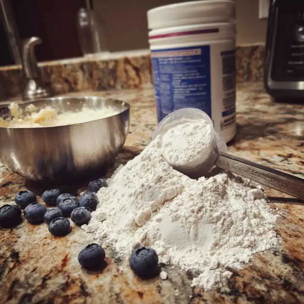 Adding protein powder to high protein blueberry muffin batter with flour measured beside it