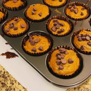 Muffin pan filled with pumpkin batter topped with chocolate chips, ready to bake high protein pumpkin muffins