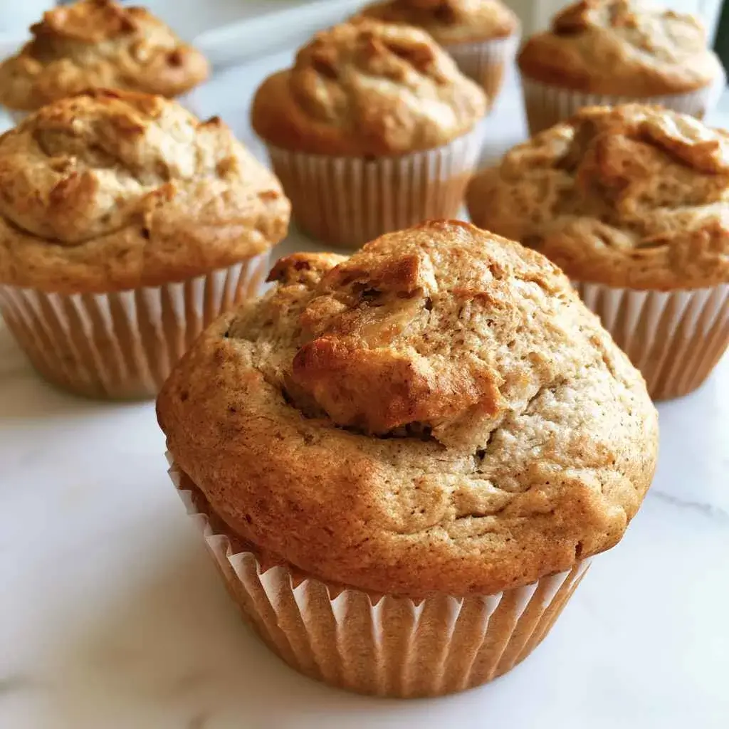 High protein banana muffins with golden cracked tops cooling on a wire rack, one split open to show a moist crumb