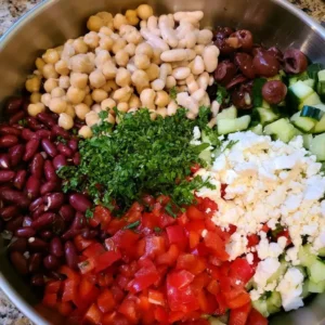 Chickpeas, beans, peppers, feta and herbs layered in a bowl for high protein bean salad