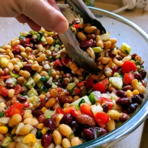 Tossing high protein bean salad with dressing in a large bowl