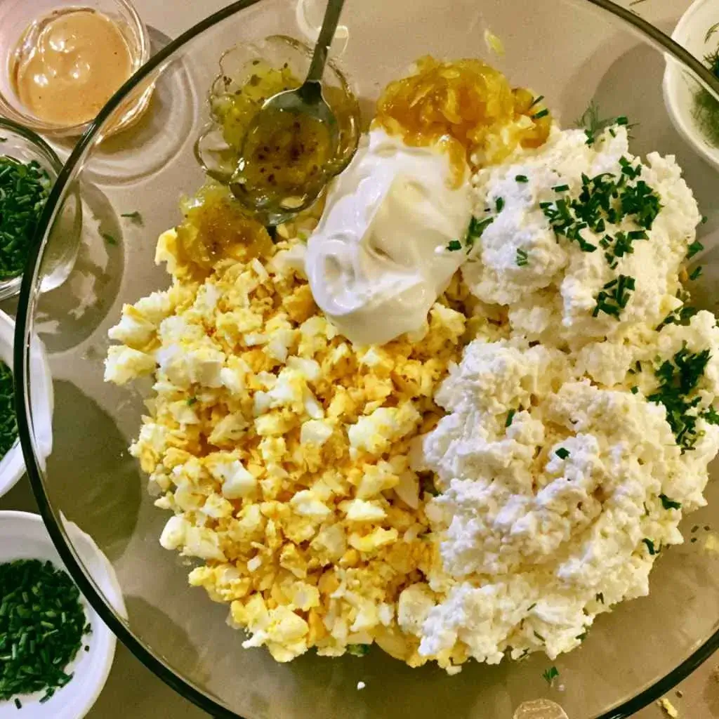 Ingredients being combined in a glass bowl to make high protein egg salad