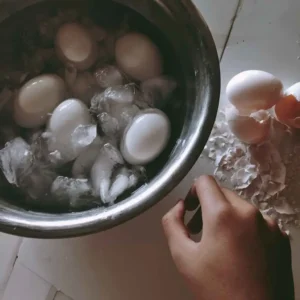 Hard-boiled eggs cooling in an ice bath and being peeled for high protein egg salad
