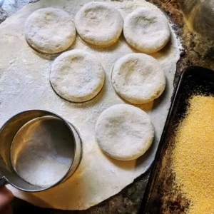 Cutting round high protein english muffin dough circles and pressing them in cornmeal