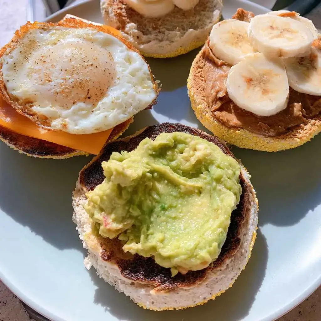 High protein english muffin halves topped with fried egg and cheese, avocado, and nut butter with banana