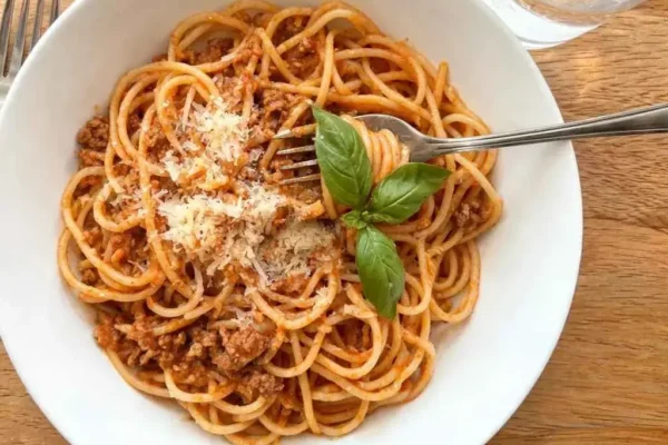 Bowl of creamy high protein spaghetti twirled on a fork with Parmesan and fresh basil