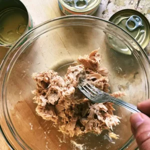 Flaking drained albacore tuna in a bowl for high protein tuna salad