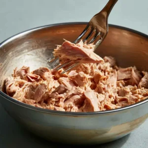 Draining canned tuna and flaking it with a fork for tuna salad with greek yogurt