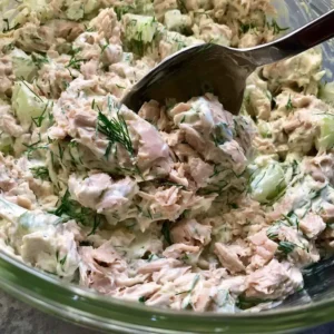 Folding together creamy tuna salad with greek yogurt in a glass bowl